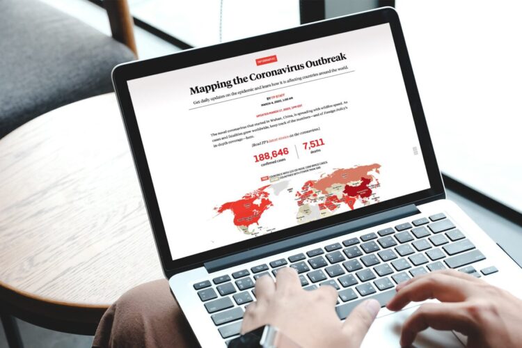 Person using a laptop displaying a coronavirus outbreak map and statistics, including total cases and deaths, with a global map in red shades highlighting affected areas.