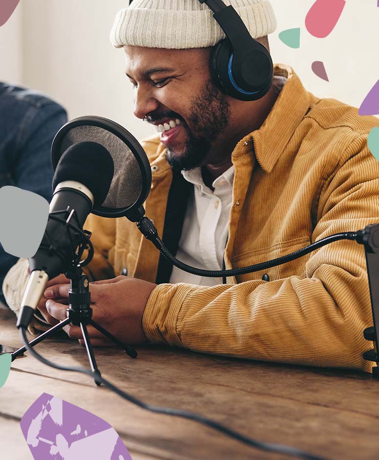 A man wearing headphones and smiling at a microphone.