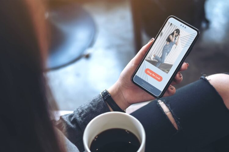 A person holding a cup of coffee uses a dating app on their smartphone, viewing a profile photo with an orange “Say Hi Now” button.