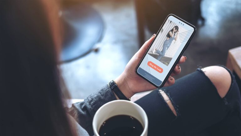 A person holding a cup of coffee uses a dating app on their smartphone, viewing a profile photo with an orange “Say Hi Now” button.