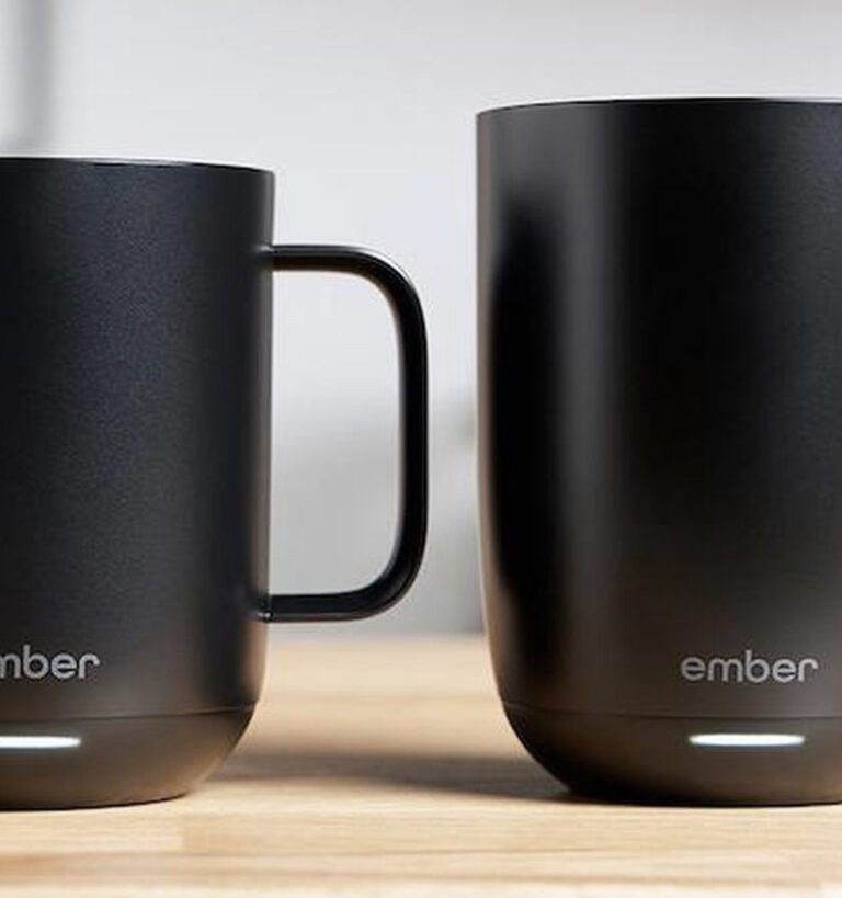 Two black Ember mugs with glowing bases are placed side by side on a wooden surface; one has a handle and the other does not.