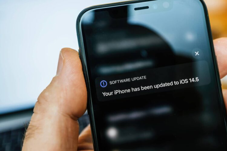 A hand holding an iPhone displaying a notification that the device has been updated to iOS 14.5.