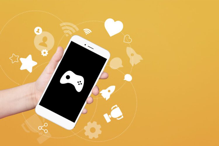 A hand holds a smartphone with a game controller icon on the screen, surrounded by white digital and gaming icons on a yellow background.