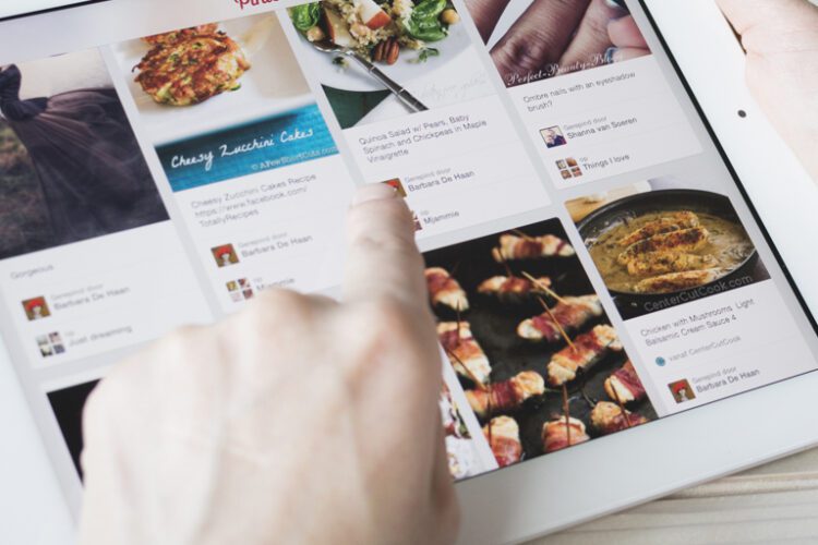 A person uses a white tablet, browsing a recipe site with various food images and descriptions displayed on the screen.