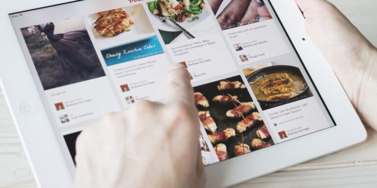 A person uses a white tablet, browsing a recipe site with various food images and descriptions displayed on the screen.