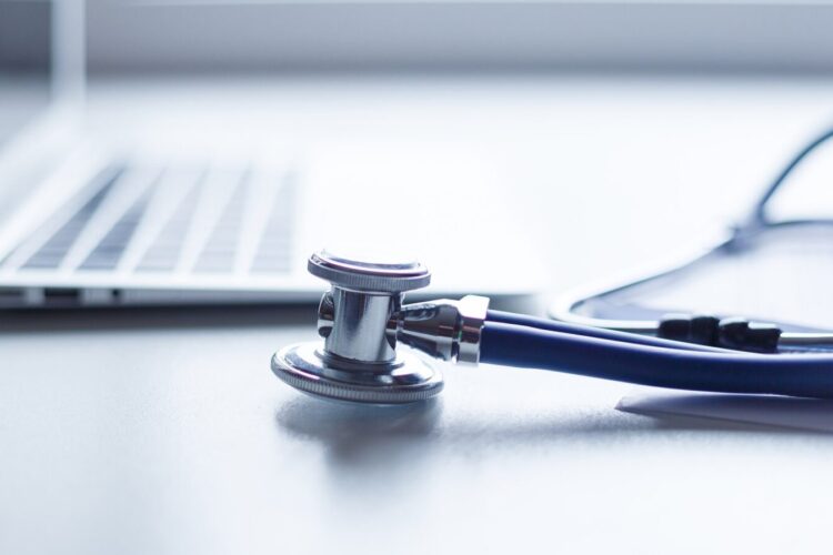 A stethoscope lies on a white surface next to an open laptop.