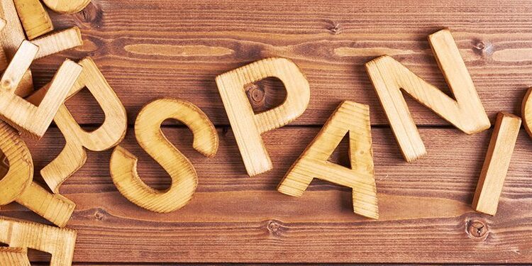 Wooden letters scattered on a wooden surface, with some arranged to spell "SPANISH" among other loose letters.