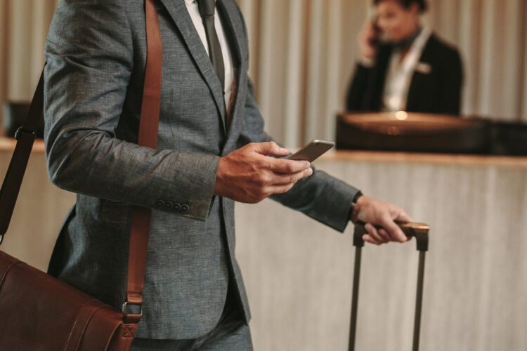 A man in a suit holding a suitcase and a phone.