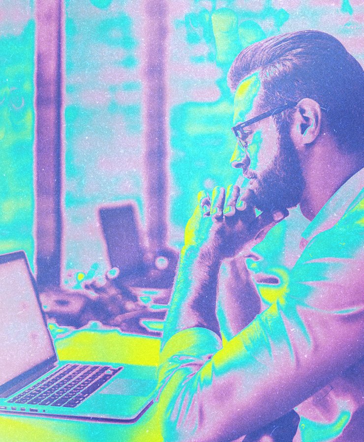 A man wearing glasses sits at a desk, looking thoughtfully at a laptop screen in a brightly colored, stylized image.