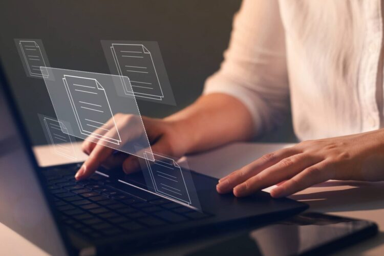 A person types on a laptop keyboard with digital file icons appearing above the screen, representing the concept of managing electronic documents.