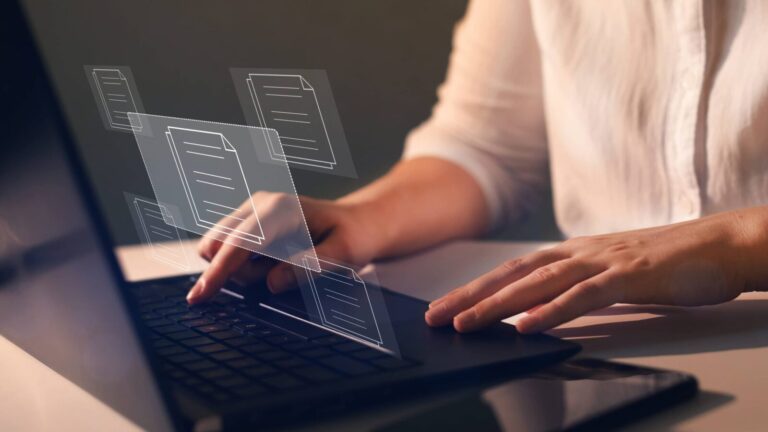 A person types on a laptop keyboard with digital file icons appearing above the screen, representing the concept of managing electronic documents.