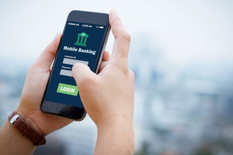 A person holds a smartphone displaying a mobile banking app login screen with fields for username and password, and a green login button.