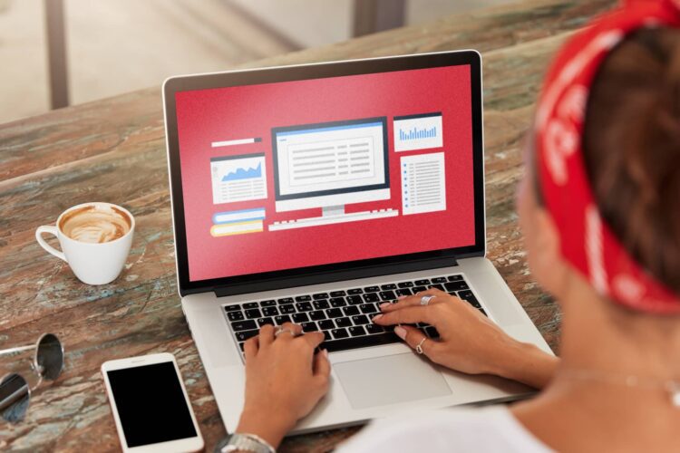 Person using a laptop with charts and graphs displayed on the screen, next to a smartphone and a cup of coffee on a wooden table.