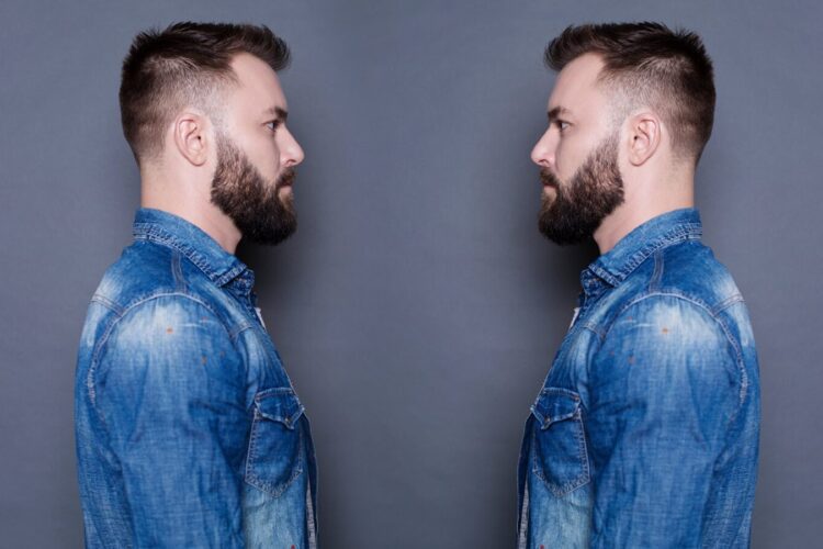 Two men with beards and denim jackets face each other against a plain gray background.