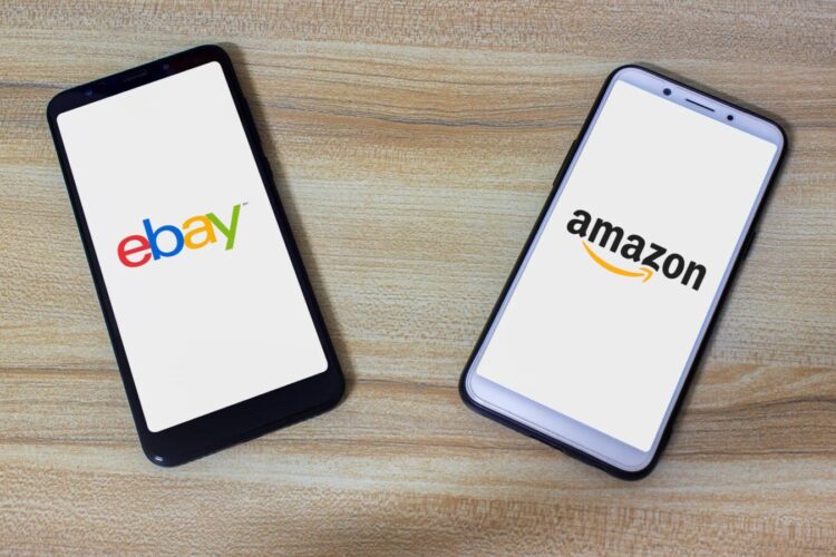 Two smartphones on a wooden surface display the eBay logo on the left and the Amazon logo on the right.