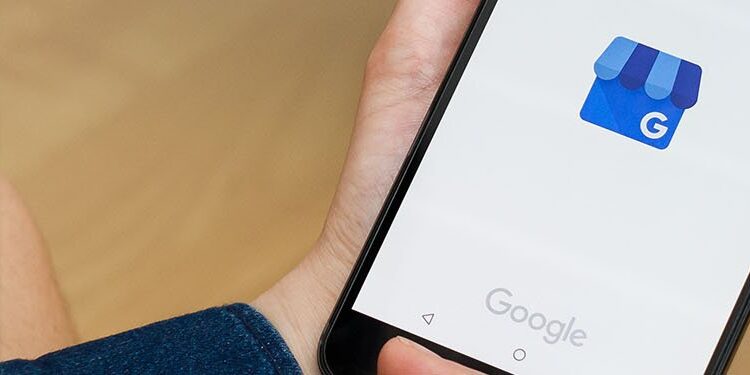 A person holding a smartphone displaying the Google My Business app logo on the screen.