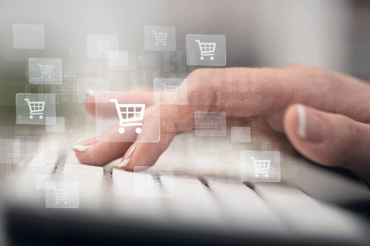 A person's hand types on a keyboard with digital shopping cart icons overlaid, representing online shopping or e-commerce.