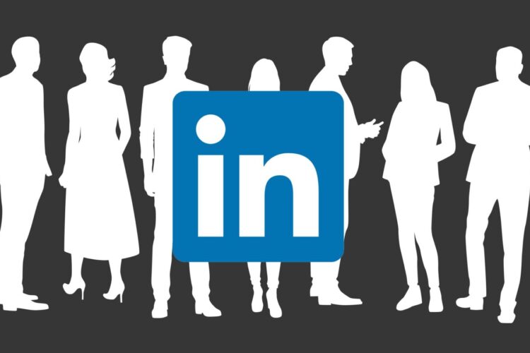Silhouettes of business people stand behind the LinkedIn logo on a dark background.