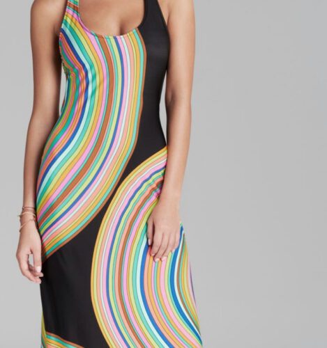 A person wearing a sleeveless black dress with bright, multicolored curved stripes stands against a plain gray background.