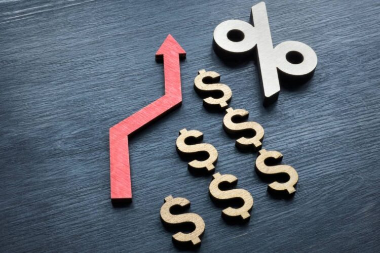 A red upward arrow, several dollar signs, and a percentage symbol arranged on a dark surface, symbolizing rising interest rates or financial growth.