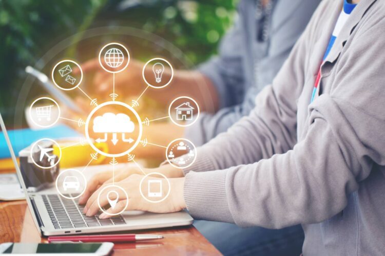 Person typing on a laptop outdoors, with digital cloud computing and internet of things (IoT) icons overlaid, representing connectivity and technology concepts.