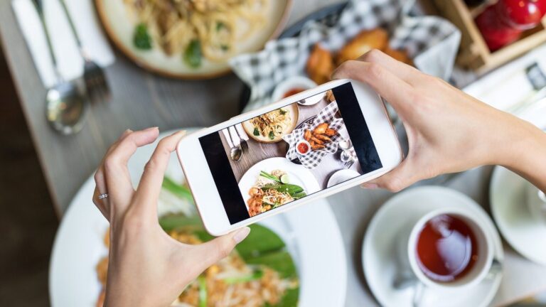 A person taking a photo of a variety of plated food and drinks on a table using a smartphone.