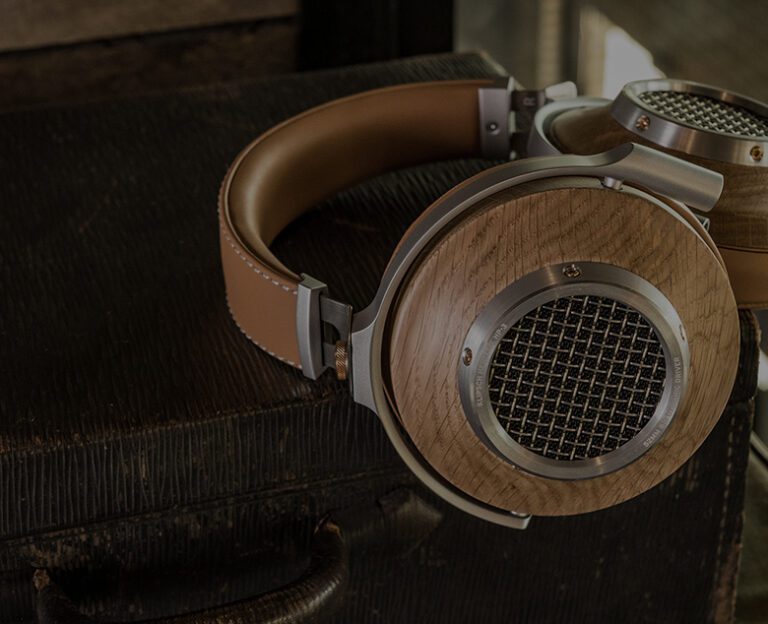 A pair of over-ear headphones with wooden ear cups and metal mesh rests on a textured, dark suitcase.