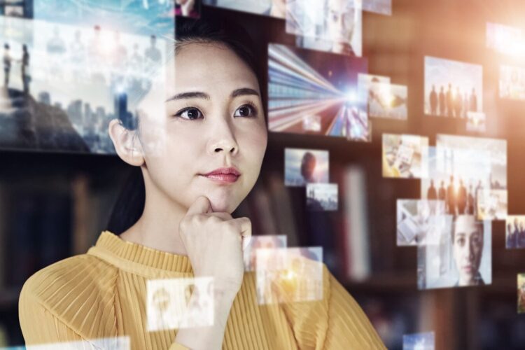 A woman in a yellow top looks thoughtfully at floating digital screens displaying various images and data, suggesting analysis or contemplation of information.