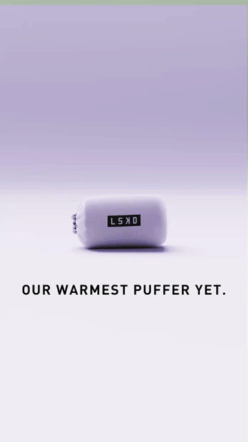 A compact, light purple puffer jacket with an LSKD label is packed into a small pouch. Black text below reads, "OUR WARMEST PUFFER YET.