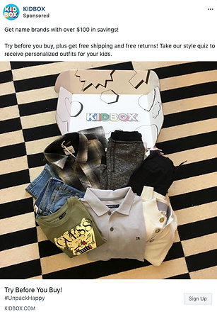 A Kidbox package on a striped rug contains kids’ clothing items, including shirts, pants, and a jacket, displayed in front of an open branded box.