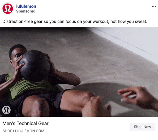 A man in athletic wear performs sit-ups while holding a medicine ball, with another person reaching toward him, on a light-colored gym floor.