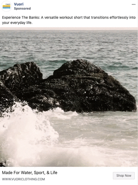 Waves crash against a large dark rock in the ocean under a cloudy sky, featured in a Vuori Clothing advertisement.