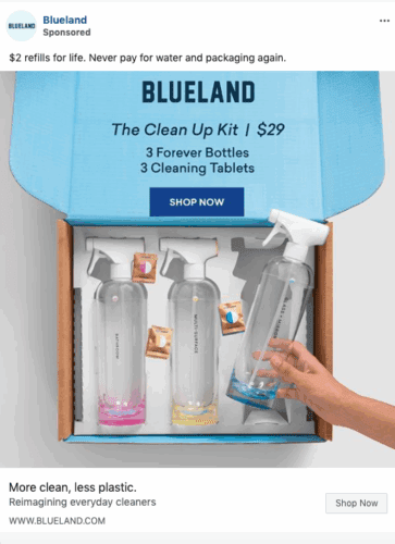 Open Blueland box showing three refillable spray bottles with colored tablets inside, labeled as “The Clean Up Kit” with a hand holding one bottle.