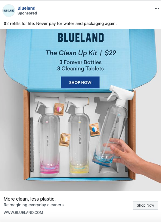 Open Blueland box showing three refillable spray bottles with colored tablets inside, labeled as “The Clean Up Kit” with a hand holding one bottle.