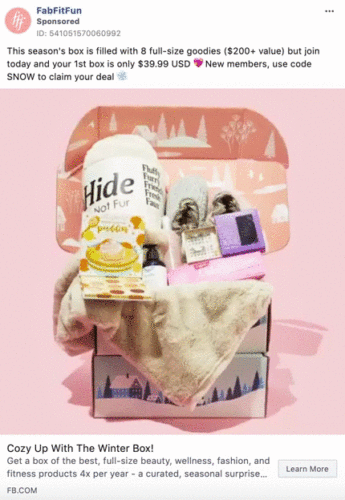 An open FabFitFun subscription box displays various items including a blanket, mug, slippers, and beauty products, all arranged on a pink background.