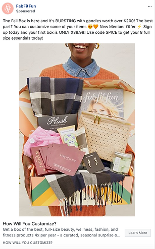 A person holds an open FabFitFun box containing a blanket, scarf, skincare items, and various beauty products.