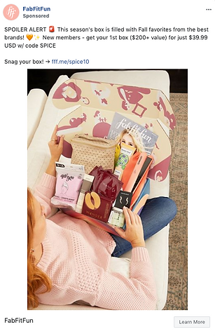 A woman sits on a bed and opens a FabFitFun subscription box filled with assorted beauty, wellness, and lifestyle products.