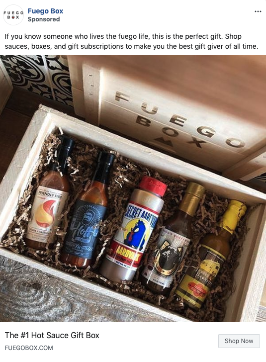 A wooden gift box with six assorted hot sauce bottles arranged on shredded paper, labeled "Fuego Box" inside the lid.