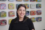 A woman with dark hair smiles at the camera while standing in front of a wall display of colorful vintage lunchboxes.