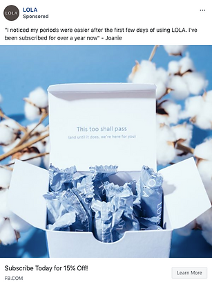 An open box of LOLA tampons sits on a white surface, with a card inside that reads, "This too shall pass," and cotton plant branches in the background.