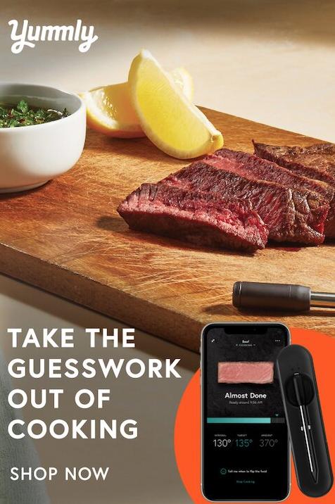 Sliced steak, lemon wedges, and a small bowl of sauce on a wooden board next to a digital meat thermometer and smartphone displaying cooking information.