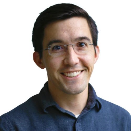 A man with short dark hair, wearing glasses and a dark button-up shirt, smiling at the camera against a plain white background.
