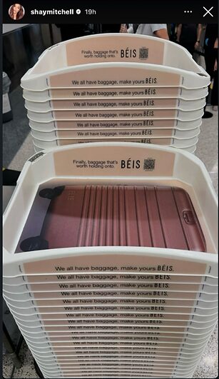 A stack of white plastic airport security trays featuring BEIS branding and an image of a brown suitcase inside the top tray.