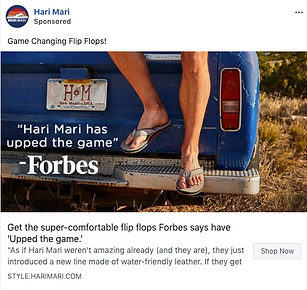 A person wearing flip flops sits on the tailgate of a blue pickup truck in a rural outdoor setting.