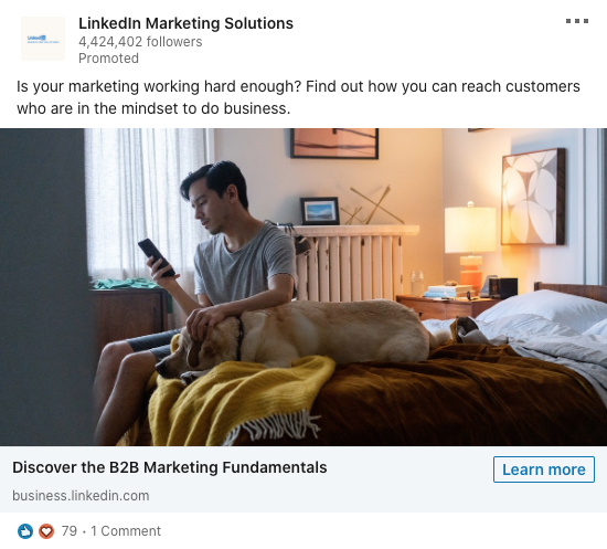 A man sits on the edge of a bed looking at his phone, with a dog lying beside him in a neatly furnished bedroom.