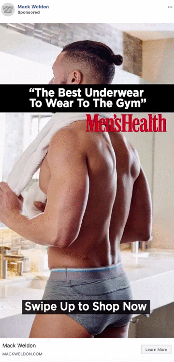 A man stands in a bathroom wearing gray boxer briefs, holding a white towel over his shoulder. Text reads, "The Best Underwear To Wear To The Gym" and "Swipe Up to Shop Now.