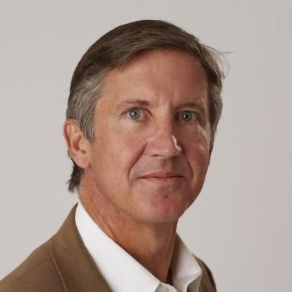 A middle-aged man with short brown hair wearing a tan blazer and white shirt, looking at the camera with a neutral expression against a plain background.