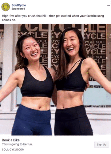 Two women in athletic wear smile and high-five in front of a SoulCycle studio.