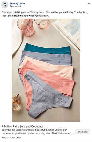 Five pairs of women's underwear in different pastel colors are neatly arranged on a white surface next to a pink candle, a glass perfume bottle, and an open book.