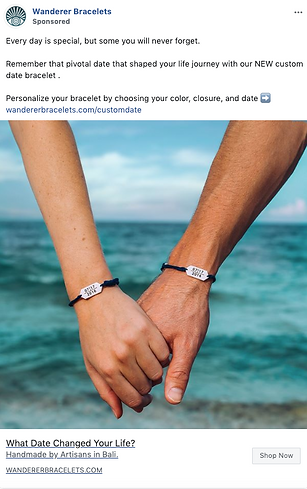 Two people holding hands, each wearing a black cord bracelet with a rectangular silver plate inscribed with a date, standing near the ocean.